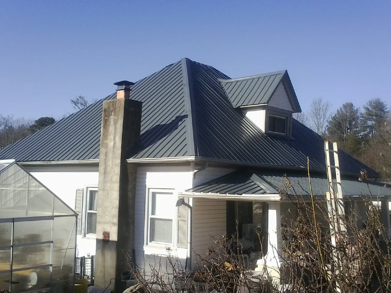 Dark blue standing seam metal roof on a white farmhouse with dormer — Slate & Tile Roof Repair by Roofing Brothers in Scotts Hill