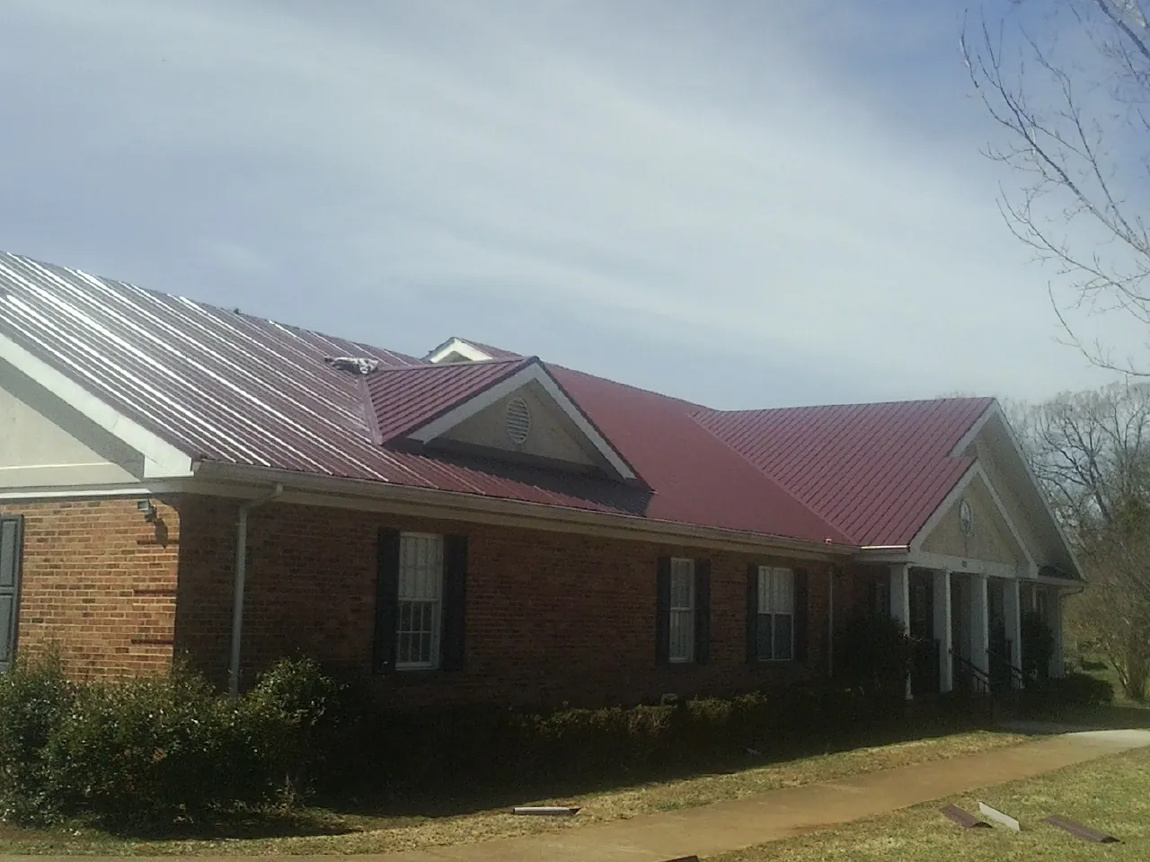 Red metal roof with gabled entries on a long brick building, from a Hail Damage Roof Repair job in Scotts Hill