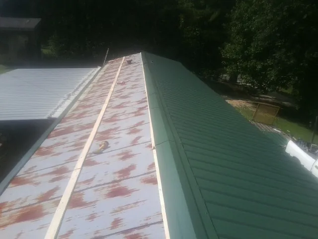 Old rusted panels beside newly installed green metal roofing — Wind Damage Roof Repair by Roofing Brothers in Scotts Hill