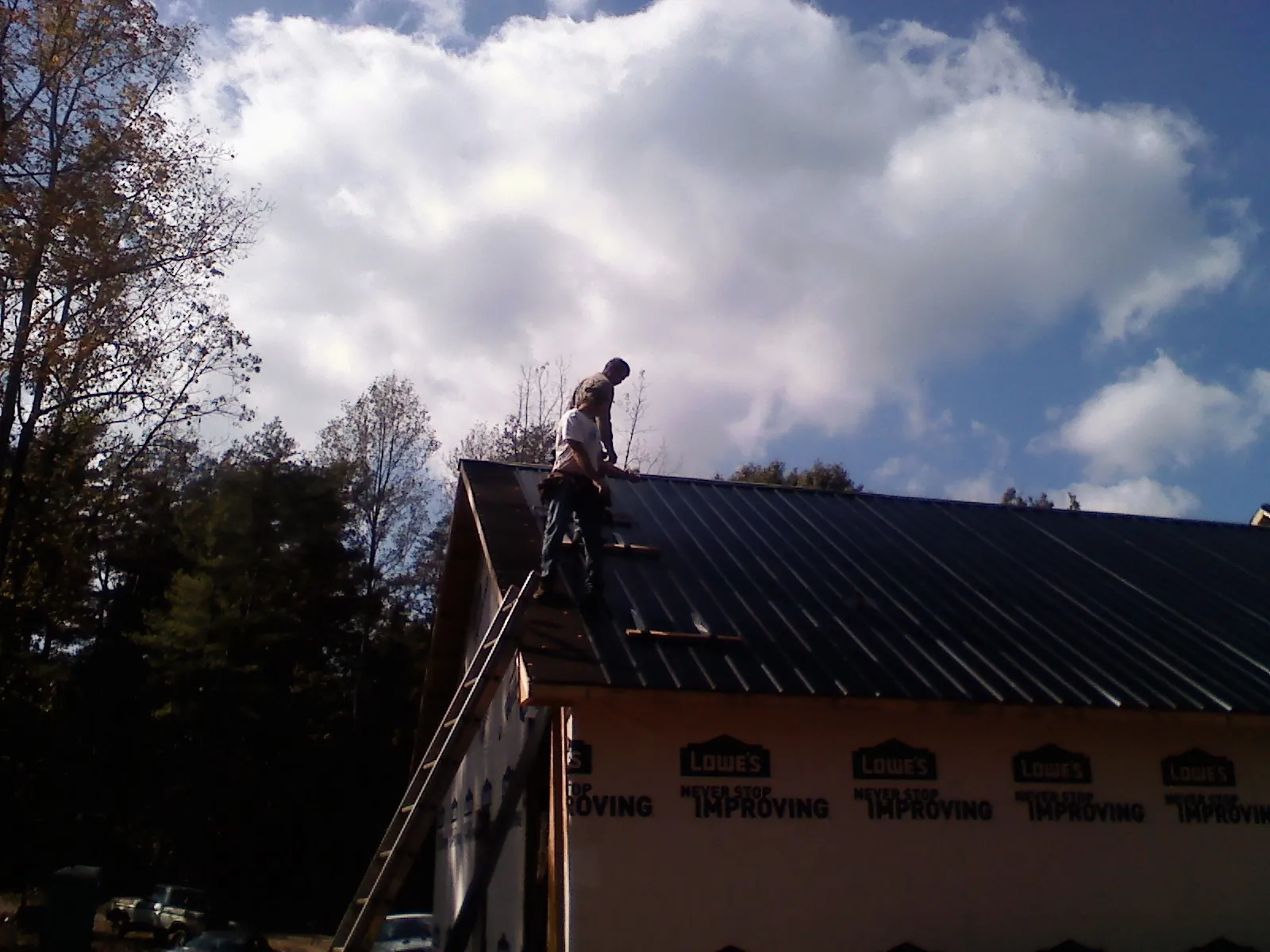 Roofer fastening dark metal panels high against a cloudy sky, from a Roof Inspection job in Scotts Hill
