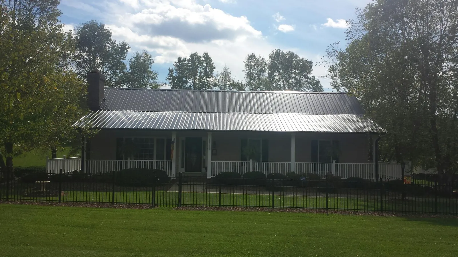 Gray metal roof on a brick ranch with a full width front porch — Gutter Guard Installation work by our crew in Scotts Hill