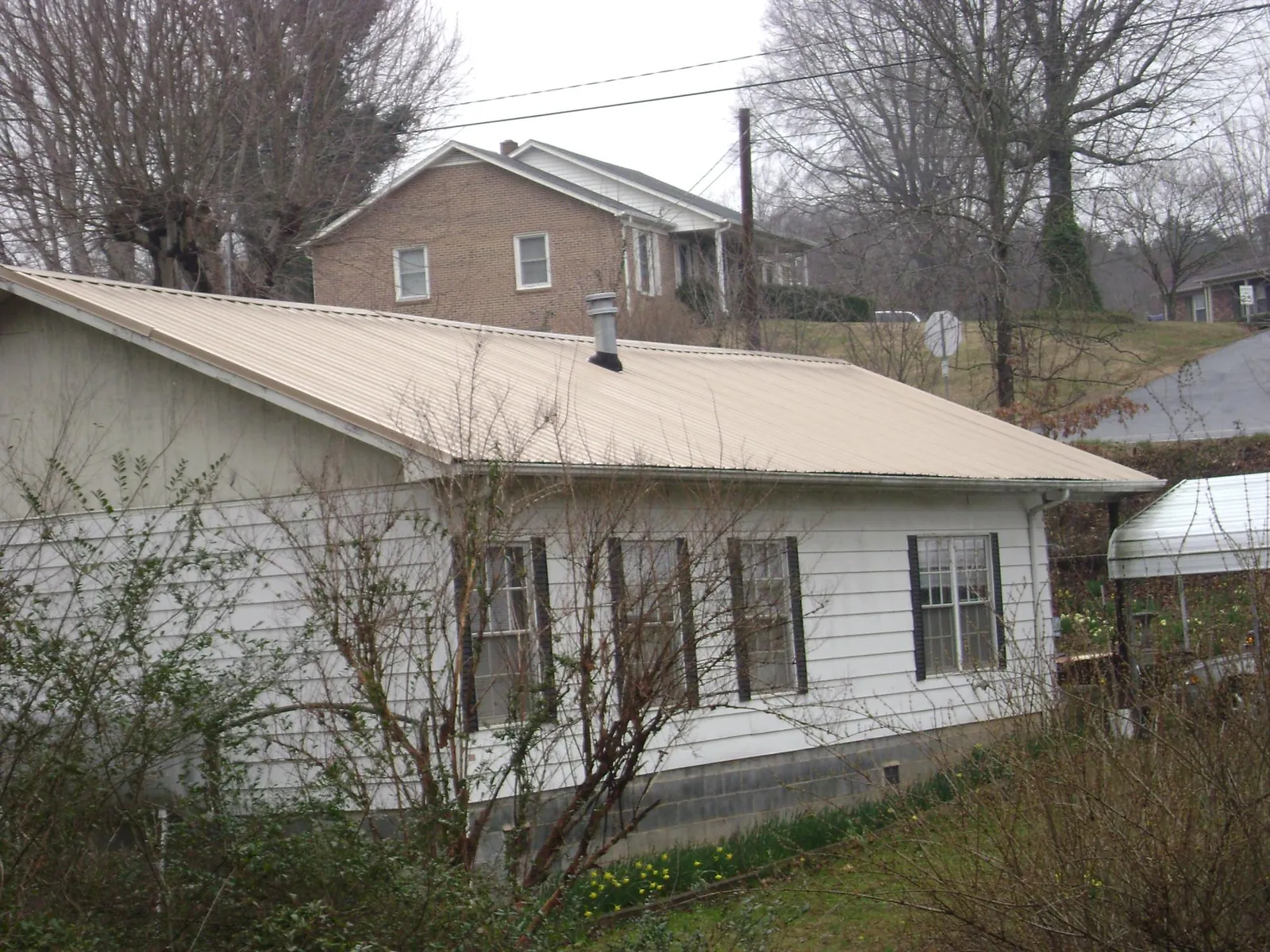 Tan metal roof on a white sided house set into a hillside — Commercial Roofing by Roofing Brothers in Scotts Hill