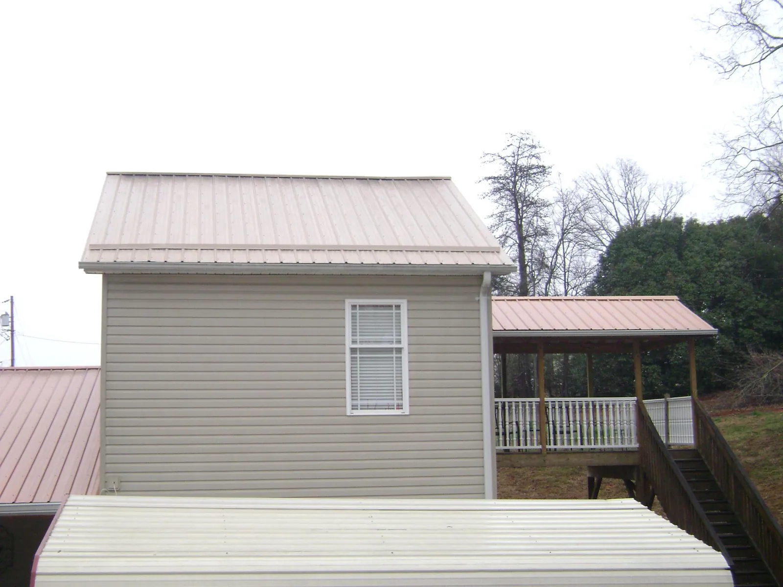 Tan metal roofs on a two story addition and attached porch, from a Roof Replacement job in Scotts Hill
